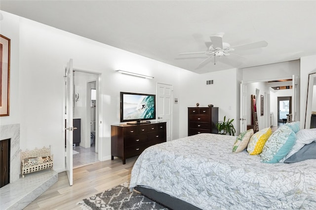 bedroom with ceiling fan, a fireplace, and light hardwood / wood-style flooring