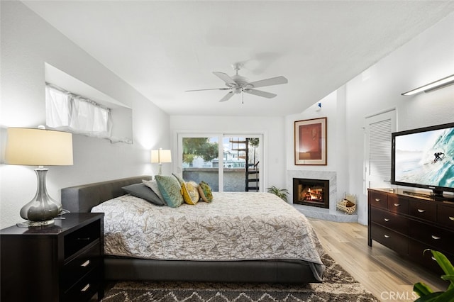 bedroom with ceiling fan, a high end fireplace, light hardwood / wood-style flooring, and access to outside