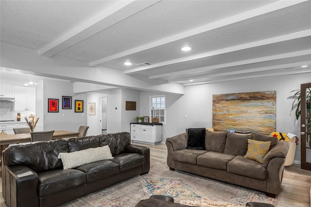 living room featuring a textured ceiling, light hardwood / wood-style floors, and beamed ceiling