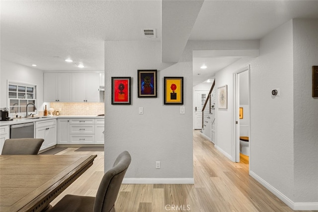 kitchen featuring white cabinetry, light hardwood / wood-style floors, backsplash, dishwasher, and sink