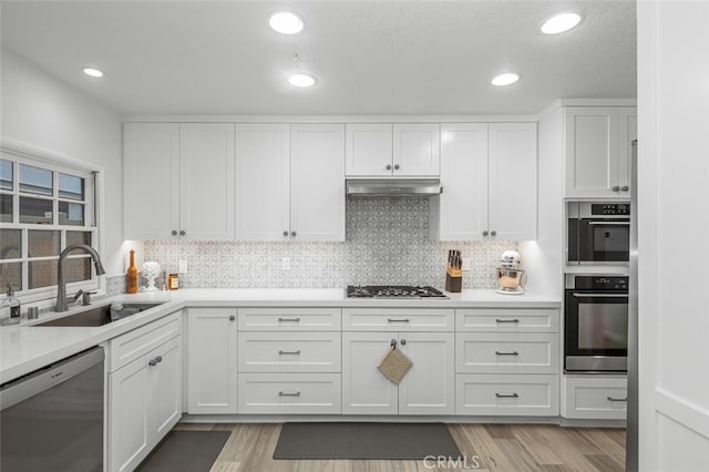 kitchen with white cabinets, appliances with stainless steel finishes, tasteful backsplash, sink, and light wood-type flooring