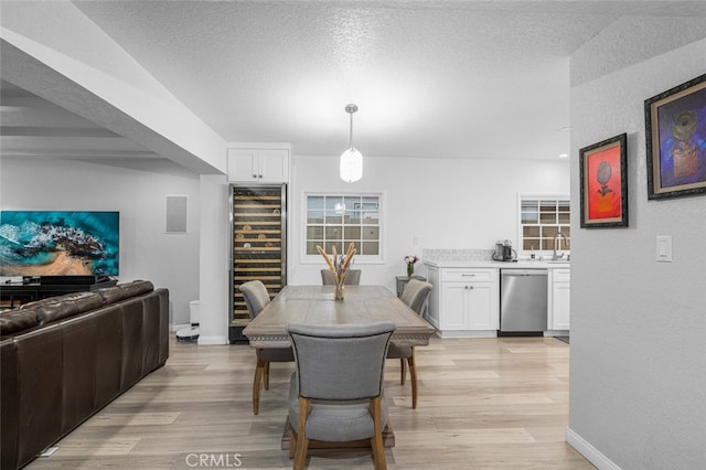 dining space featuring light hardwood / wood-style floors, a textured ceiling, and wine cooler