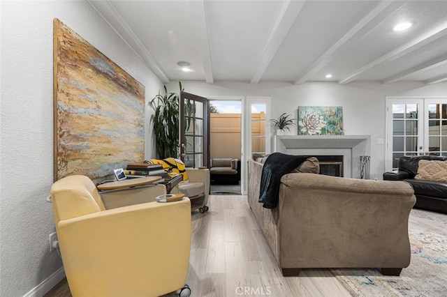 living room with beam ceiling, a healthy amount of sunlight, french doors, and light hardwood / wood-style floors