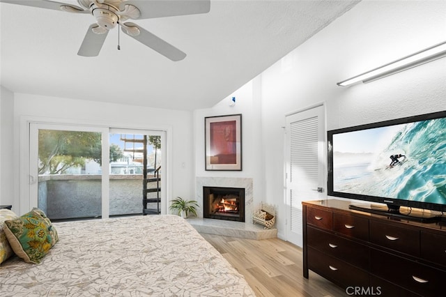 bedroom featuring ceiling fan, access to outside, light wood-type flooring, a premium fireplace, and lofted ceiling