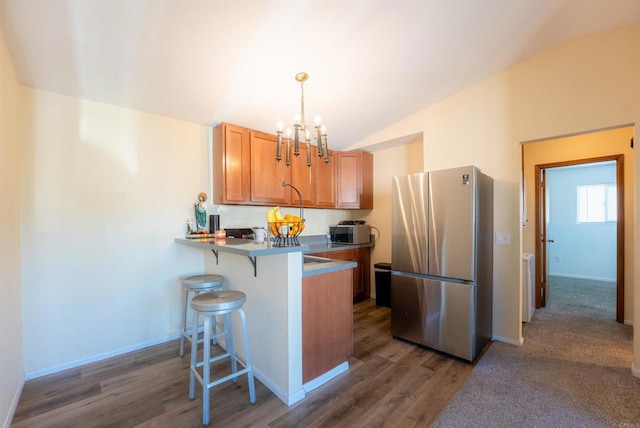 kitchen featuring lofted ceiling, pendant lighting, kitchen peninsula, a kitchen breakfast bar, and stainless steel fridge