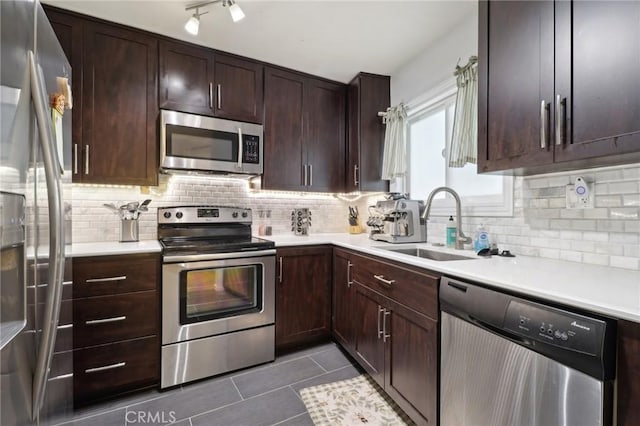 kitchen featuring dark tile patterned flooring, appliances with stainless steel finishes, sink, backsplash, and dark brown cabinets