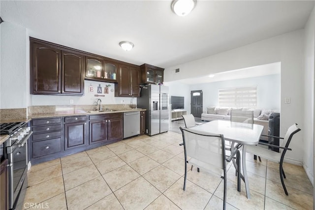 kitchen featuring appliances with stainless steel finishes, light tile patterned flooring, light stone countertops, dark brown cabinetry, and sink