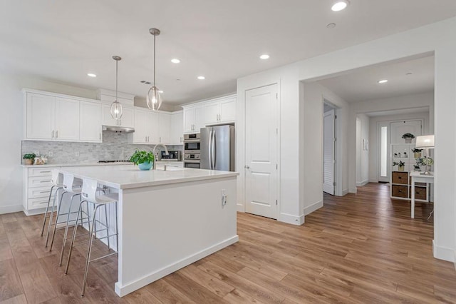 kitchen with white cabinetry, decorative light fixtures, a center island with sink, light wood-type flooring, and stainless steel refrigerator