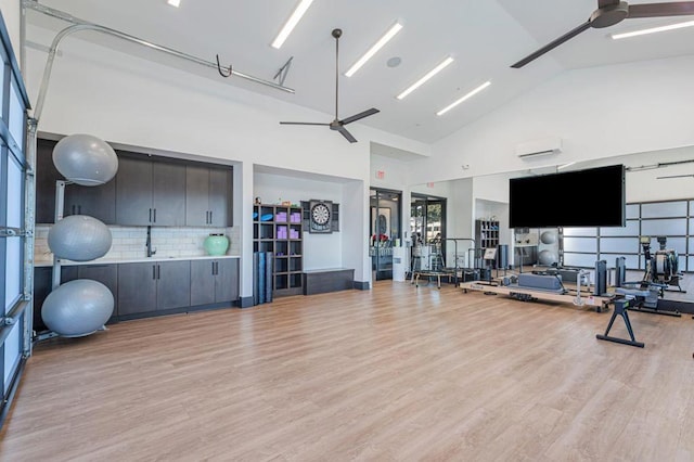 workout area with sink, ceiling fan, high vaulted ceiling, a wall mounted AC, and light wood-type flooring