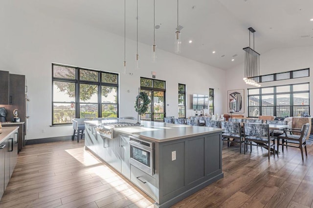 kitchen featuring high vaulted ceiling, decorative light fixtures, stainless steel gas cooktop, a large island, and light hardwood / wood-style floors