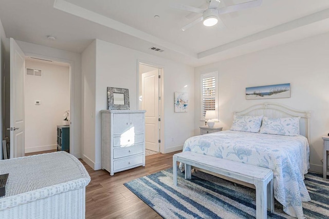 bedroom with light hardwood / wood-style floors, ceiling fan, and a tray ceiling