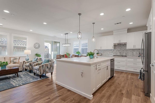 kitchen with hanging light fixtures, a center island with sink, and white cabinets