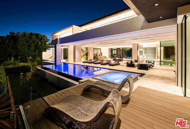 pool at night featuring an outdoor hangout area, a deck, and an in ground hot tub