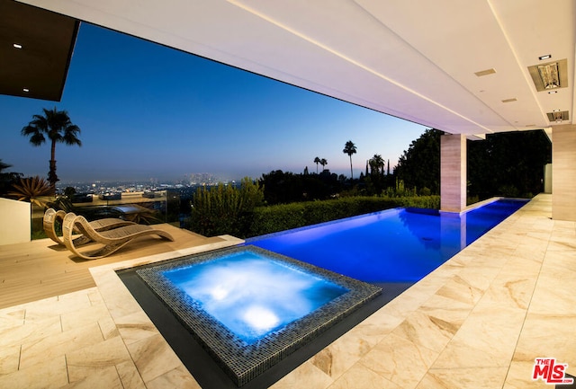 pool at dusk featuring an in ground hot tub