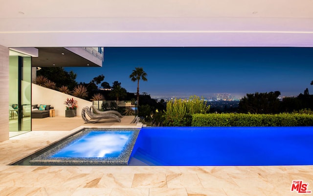 pool at dusk featuring an in ground hot tub and a patio