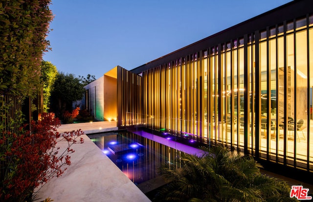 pool at dusk featuring a patio and an in ground hot tub