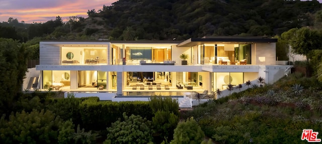 back house at dusk with outdoor lounge area, a balcony, and a patio