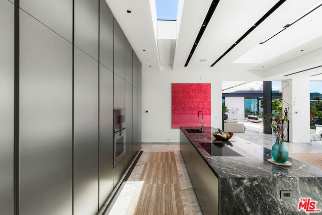 kitchen with sink, stainless steel oven, a skylight, dark stone counters, and black electric cooktop