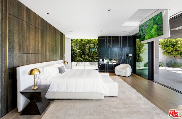 bedroom with floor to ceiling windows, access to exterior, and light wood-type flooring