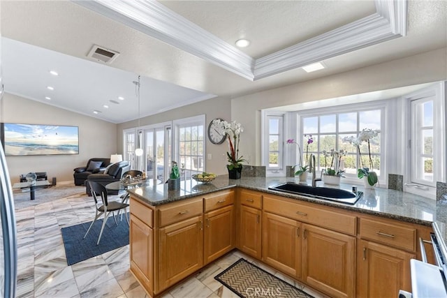 kitchen featuring kitchen peninsula, a tray ceiling, dark stone counters, crown molding, and sink