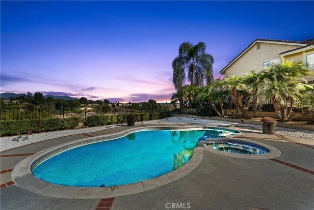 pool at dusk with an in ground hot tub and a patio