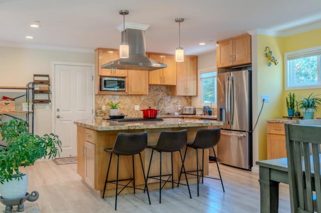 kitchen featuring light hardwood / wood-style floors, stainless steel appliances, light brown cabinetry, hanging light fixtures, and wall chimney range hood