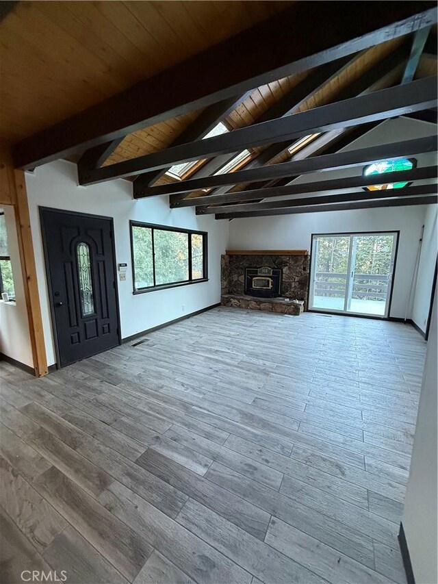 unfurnished living room featuring hardwood / wood-style flooring, lofted ceiling with beams, a stone fireplace, and a healthy amount of sunlight