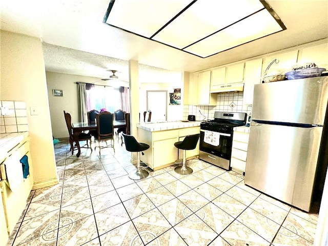 kitchen featuring tasteful backsplash, ceiling fan, tile countertops, appliances with stainless steel finishes, and a textured ceiling