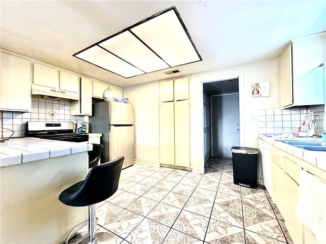 kitchen with stove, tile counters, tasteful backsplash, and stainless steel refrigerator