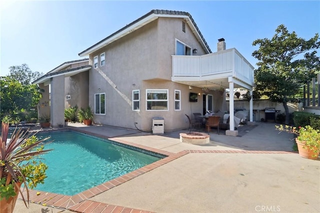 rear view of property with a balcony, a patio area, and an outdoor fire pit