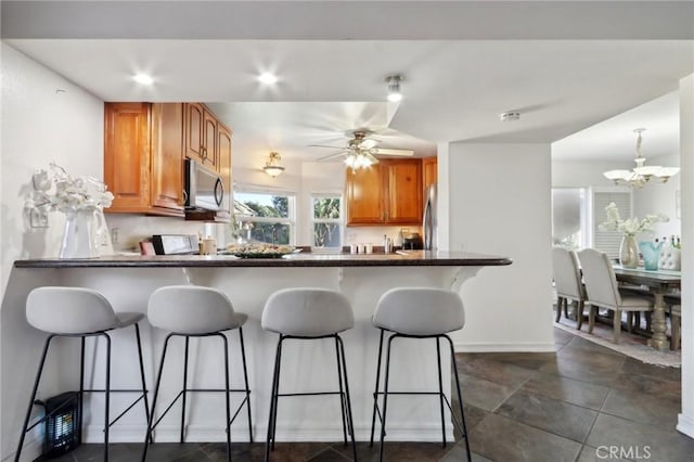 kitchen with stainless steel appliances, a kitchen bar, kitchen peninsula, and ceiling fan with notable chandelier