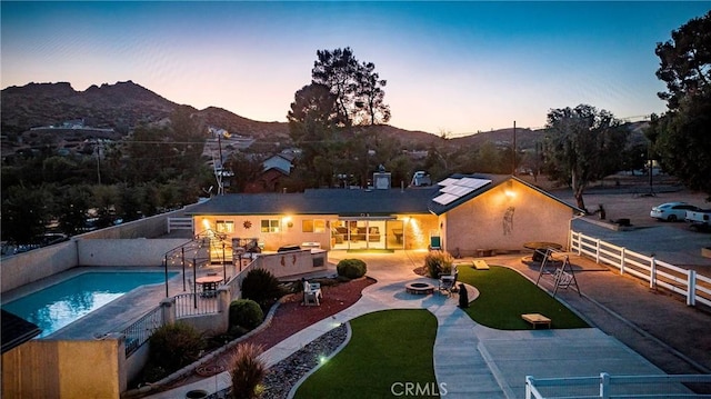 back house at dusk with a mountain view, a patio area, and a fenced in pool