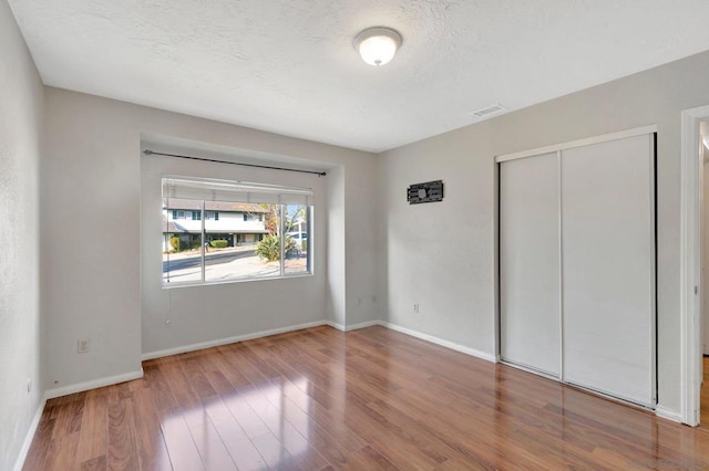 unfurnished bedroom with a textured ceiling, a closet, and wood-type flooring