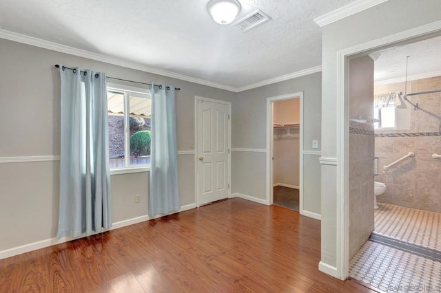 unfurnished bedroom with a walk in closet, crown molding, and multiple windows