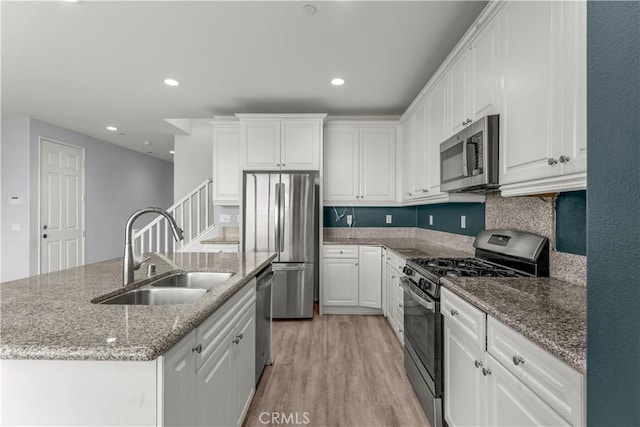 kitchen with stone counters, white cabinetry, sink, stainless steel appliances, and a center island with sink