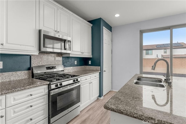 kitchen featuring stainless steel appliances, white cabinetry, sink, and dark stone countertops