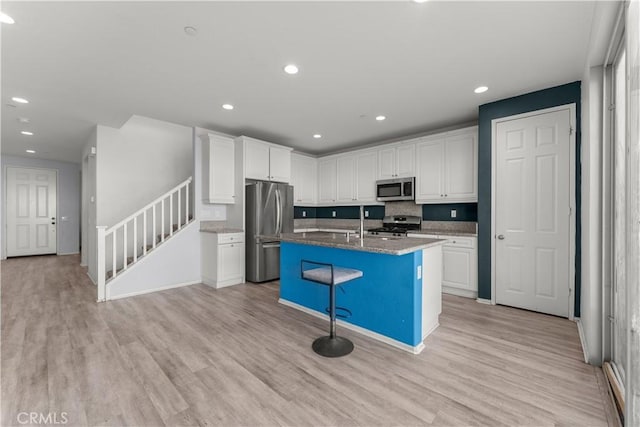 kitchen with a kitchen island with sink, white cabinetry, a kitchen bar, stainless steel appliances, and stone countertops