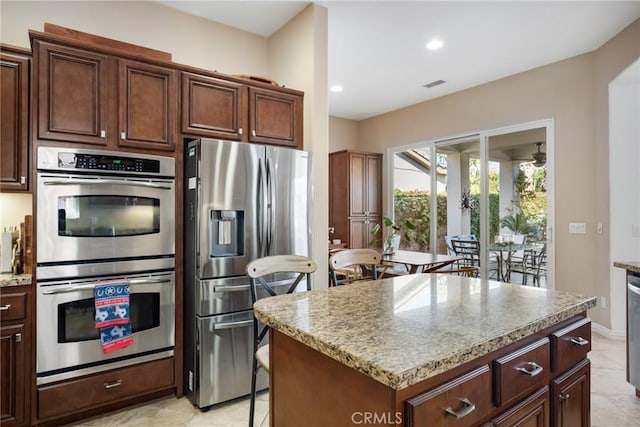 kitchen with light tile patterned floors, stainless steel appliances, a kitchen island, and light stone countertops