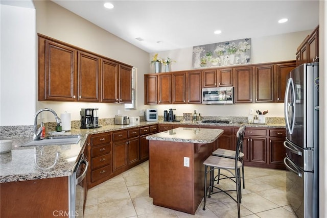 kitchen with a kitchen island, sink, light stone countertops, a breakfast bar area, and stainless steel appliances