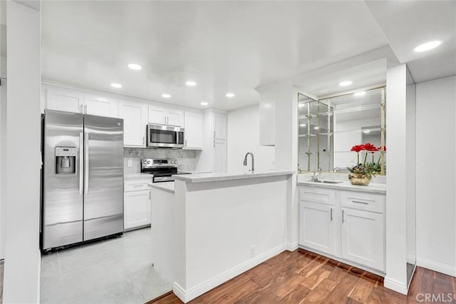 kitchen with kitchen peninsula, appliances with stainless steel finishes, backsplash, white cabinets, and light hardwood / wood-style flooring