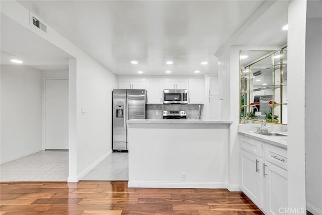 kitchen featuring kitchen peninsula, decorative backsplash, sink, appliances with stainless steel finishes, and white cabinets