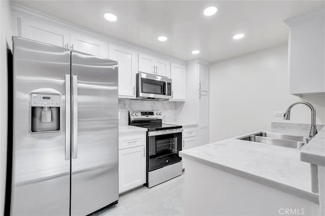 kitchen featuring stainless steel appliances, backsplash, white cabinets, light stone counters, and sink