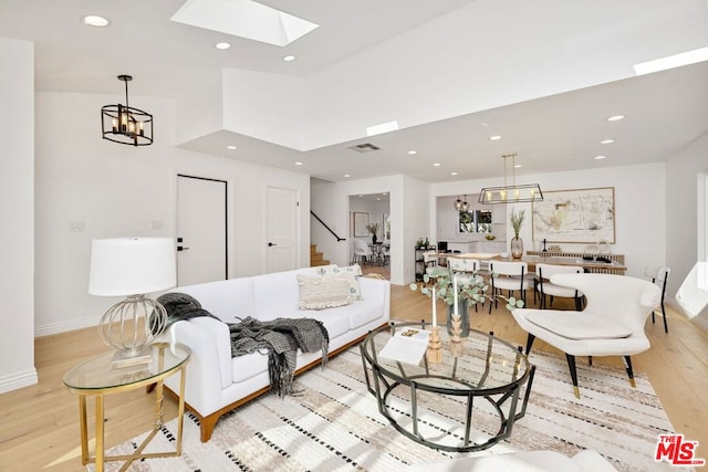 living room featuring a high ceiling, an inviting chandelier, a skylight, and light wood-type flooring