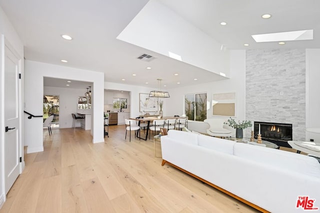 living room with a fireplace, a skylight, and light wood-type flooring