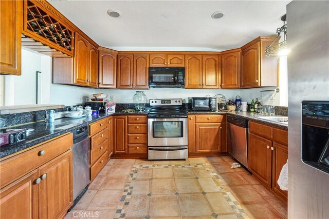 kitchen featuring light tile patterned floors, appliances with stainless steel finishes, decorative light fixtures, dark stone counters, and sink