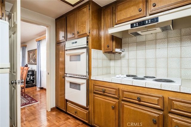 kitchen featuring light parquet floors, white appliances, tile counters, and tasteful backsplash