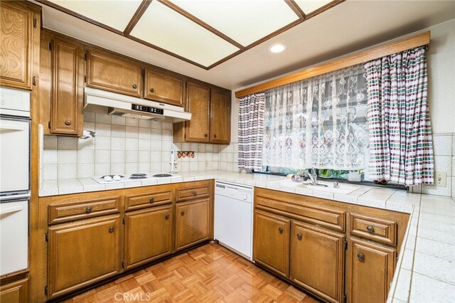 kitchen featuring light parquet floors, tile counters, sink, and white appliances