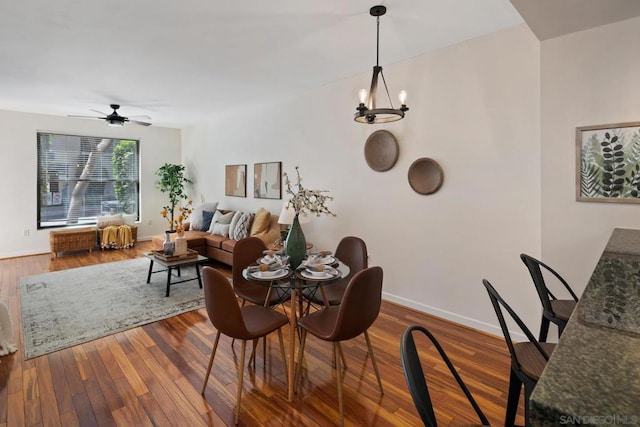 dining space with ceiling fan with notable chandelier and hardwood / wood-style flooring