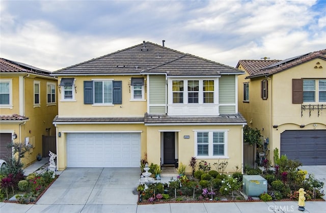 view of property with stucco siding, a tiled roof, driveway, and a garage