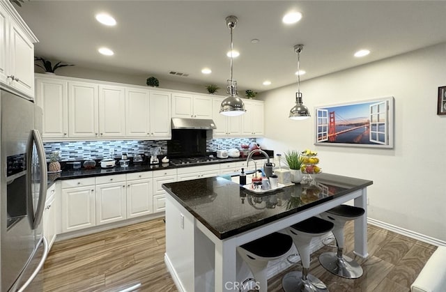 kitchen with visible vents, gas stovetop, under cabinet range hood, a kitchen bar, and stainless steel fridge